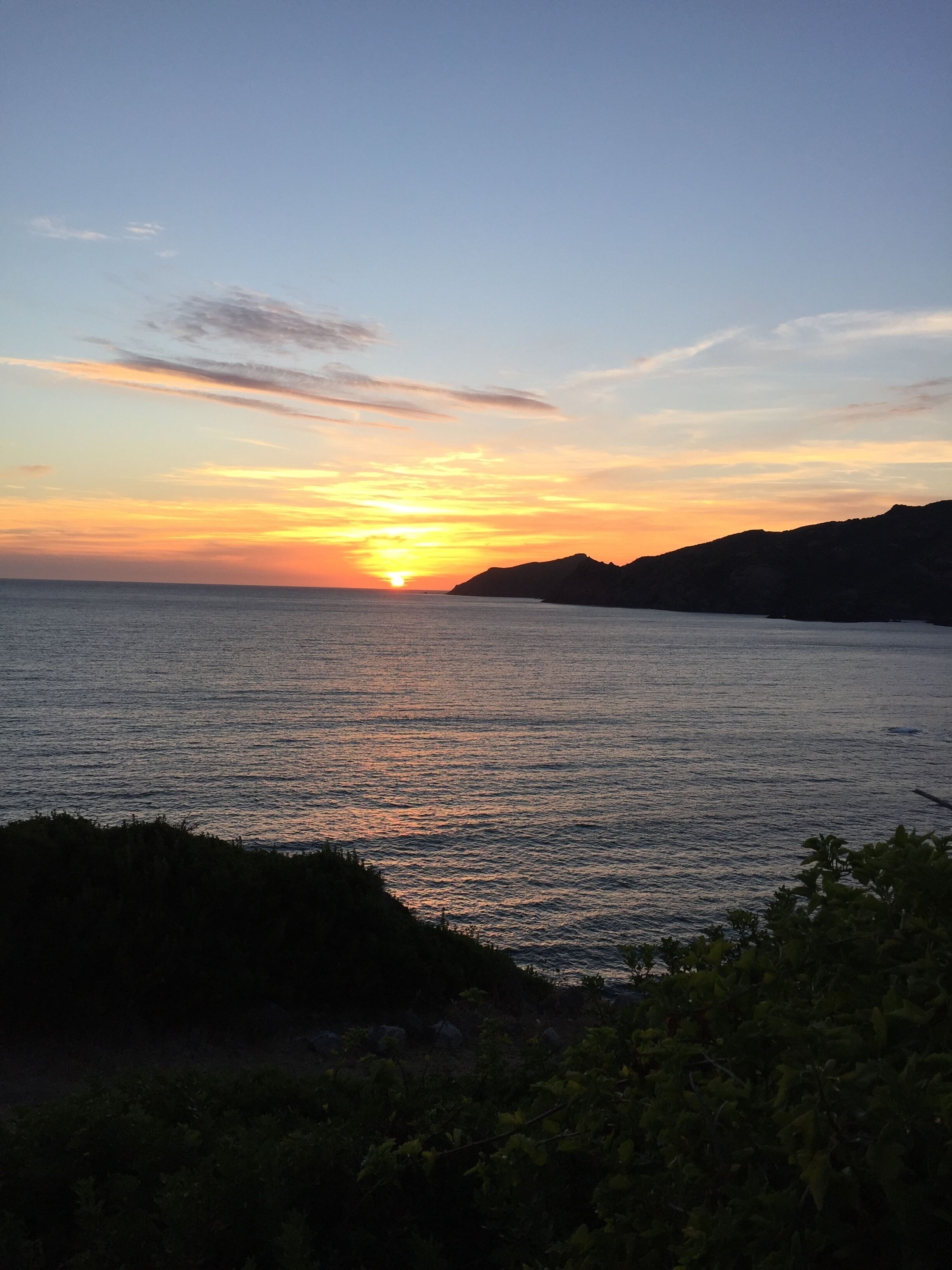 Ein Sonnenuntergang über ruhigem Meer mit weit entfernten Landformen.