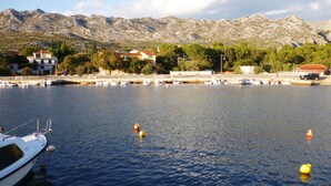 A marina with boats docked, a mountain range in the background, and buildings along the shore.