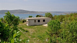 A small, single-story building with a flat roof, surrounded by greenery and overlooking a body of water.