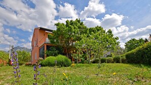 A red building with a sloped roof, surrounded by lush greenery and flowering plants.