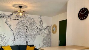 Una sala de estar moderna con un sofá, una mesa de centro y taburetes de bar. Hay un mural de un mapa del mundo en la pared y un reloj.