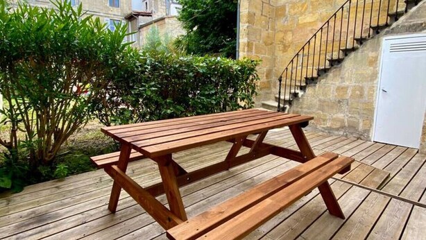 Una mesa de picnic de madera en un muelle de madera, con un muro de piedra y una escalera.