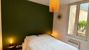 Un dormitorio con cama, lámpara colgante, ventana y radiador fijado a la pared.