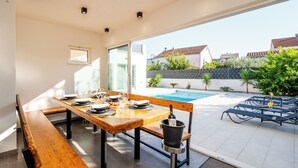 A dining area with a pool view, wooden table, and outdoor seating. - Blue fantasy is new modern villa 5 min from the beach! (Kaštel Novi)