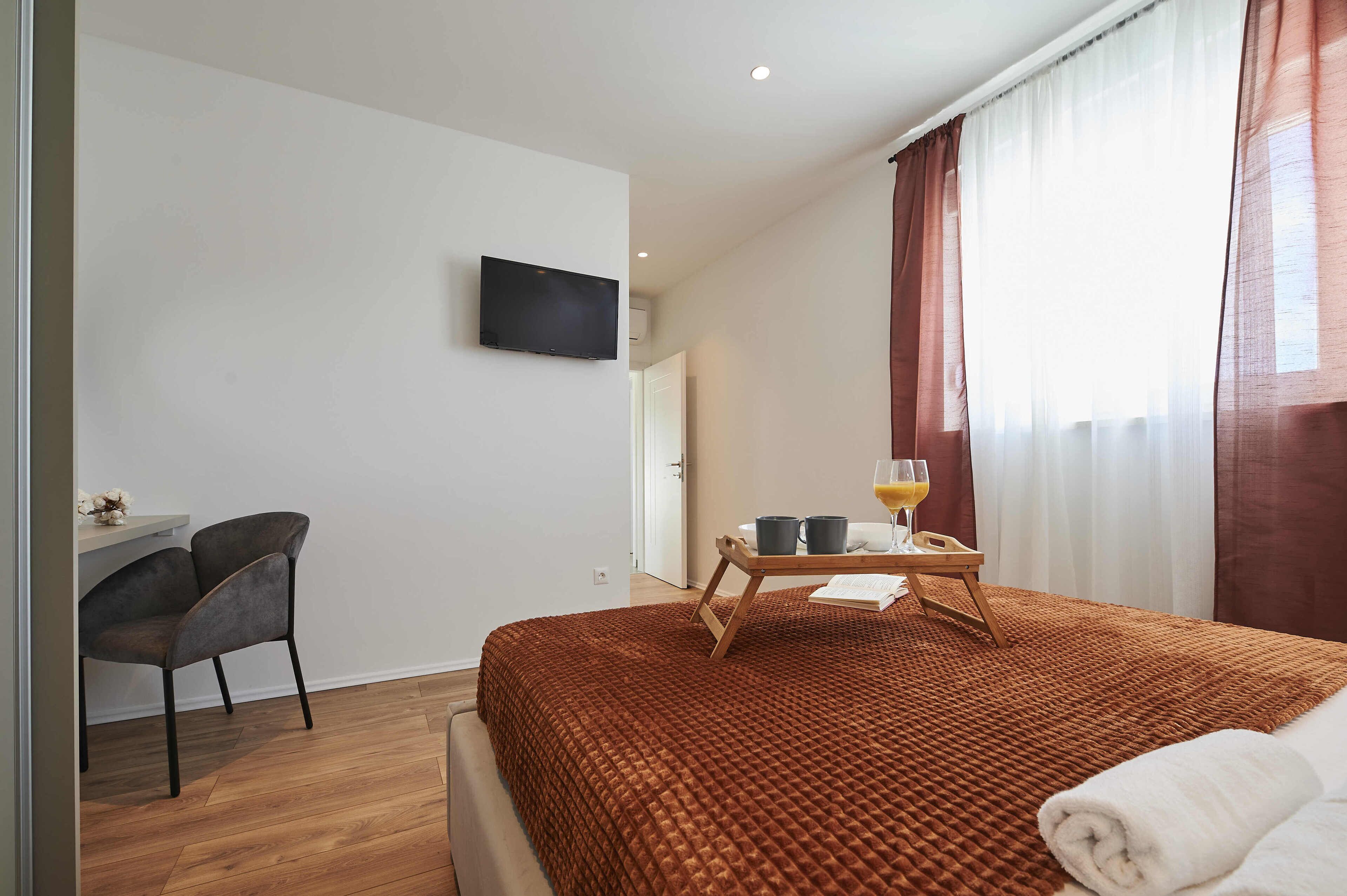 A hotel room with a bed, a desk, a chair, a TV, and a window with curtains.