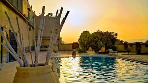 A swimming pool with a tiled edge, a large planter with sticks, and a building with a flat roof in the background. - Maisonette with terrace in riad with swimming pool and farmhouse (Taroudant)