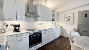 A modern kitchen with white cabinetry, a built-in oven, a coffee machine, and a stainless steel range hood. - London Warehouse One Bedroom Apt (London)