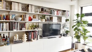 A well-organized living room with a large flat-screen TV, multiple bookshelves filled with books and decorative items, and a potted plant. - London Warehouse One Bedroom Apt (London)