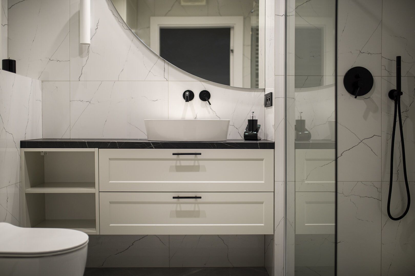 A modern bathroom with a white marble sink, black countertop, and a glass shower enclosure.