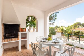 A patio area with a brick fireplace, white chairs, and a table set for dining.