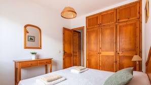 Ein Schlafzimmer mit Bett, Holzschrank, Schreibtisch mit Pflanze und Spiegel an der Wand.