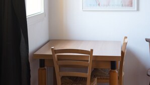 Un coin repas avec une table et des chaises en bois, une affiche encadrée au mur et une fenêtre avec un rideau.
