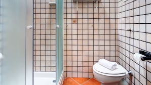 Une salle de bain avec une douche à parois de verre, des toilettes, un lavabo et une étagère contenant des articles de toilette.