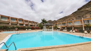 Una piscina rodeada de edificios de hotel con balcones y montañas al fondo.