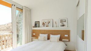 Un dormitorio con una cama grande, un cabecero de madera, una mesita de noche pequeña y una ventana con cortinas.
