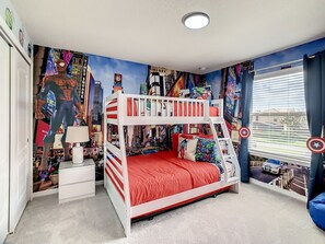 A bunk bed with a red mattress, a nightstand with a lamp, and a wall mural of a cityscape.