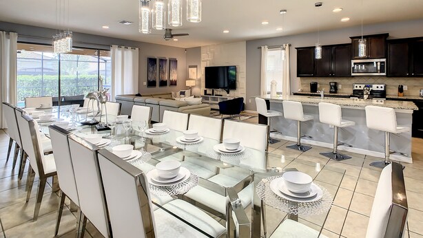 Una cocina moderna con armarios oscuros, una isla grande y un comedor con mesas de vidrio y sillas blancas.
