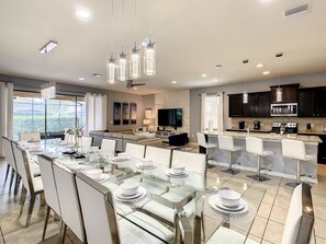 A modern kitchen with dark cabinets, a large island, and a dining area with glass tables and white chairs.