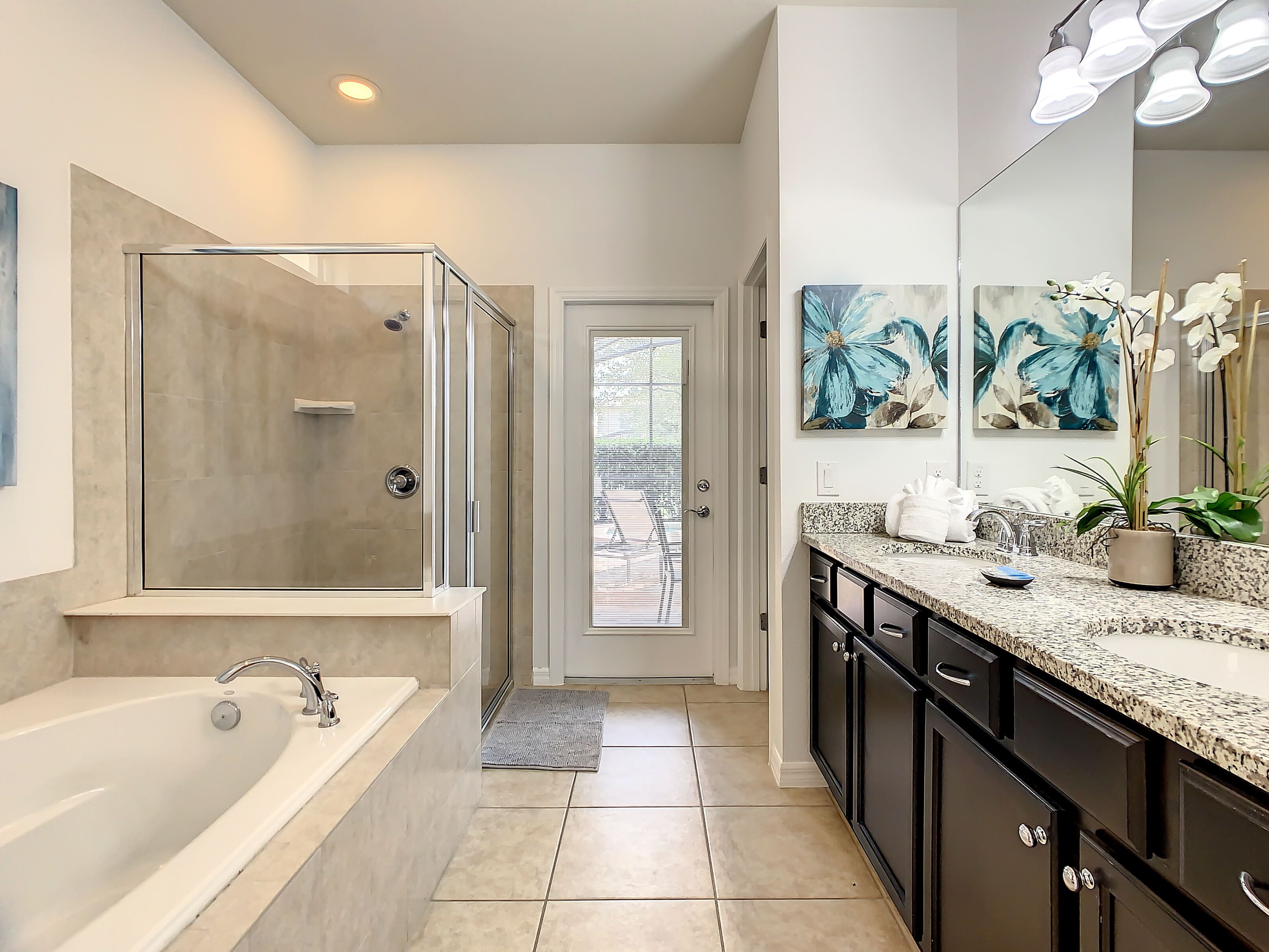A modern bathroom with a walk-in shower, a large bathtub, and a granite countertop with a sink and mirror.