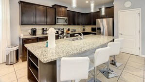 Una cocina moderna con armarios de madera oscura, electrodomésticos de acero inoxidable, encimera de granito e iluminación colgante.