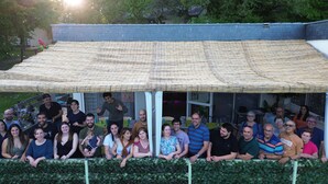 A group of people gathered under a covered area with a brick wall and greenery in the background. - Kamea Club La Gironie (Turenne)