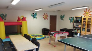 A room with a foosball table, ping pong table, and a ball pit. There are chairs and a table with a tablecloth. - Kamea Club La Gironie (Turenne)