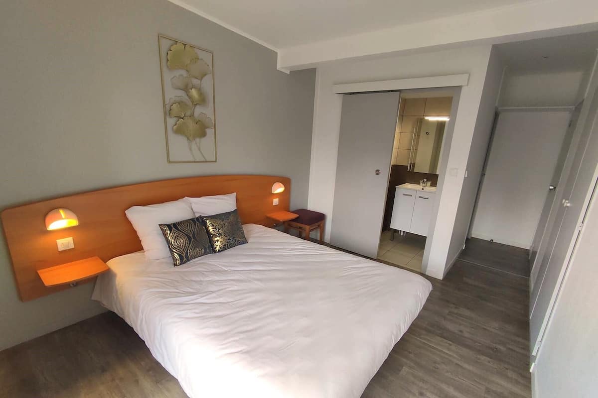 Een keurig opgemaakt bed met witte lakens, decoratieve kussens, een houten hoofdbord en nachtlampjes.
