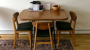 A dining area with a wooden table and chairs, framed artwork on the wall, a menu stand, and a decorative bowl.