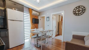 A modern kitchen with a built-in refrigerator, a dining area with a table and chairs, and a living area with a sofa. - Umut Apartments (Trabzon)