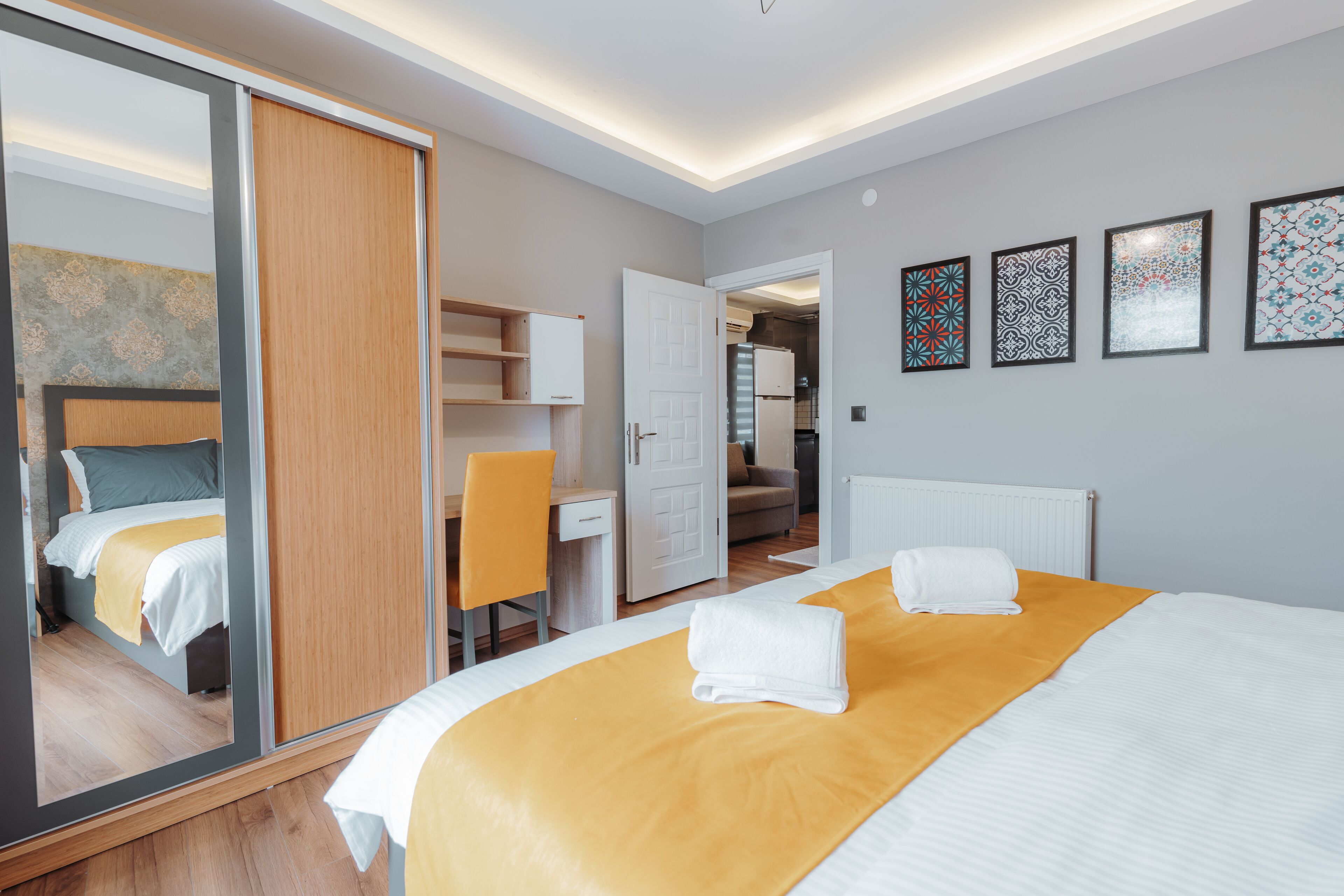 A modern hotel room with a large bed, a desk, a chair, and a wardrobe.