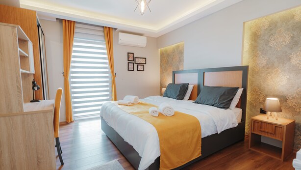 A modern bedroom with a large bed, a desk, and a nightstand. - Umut Apartments (Trabzon)