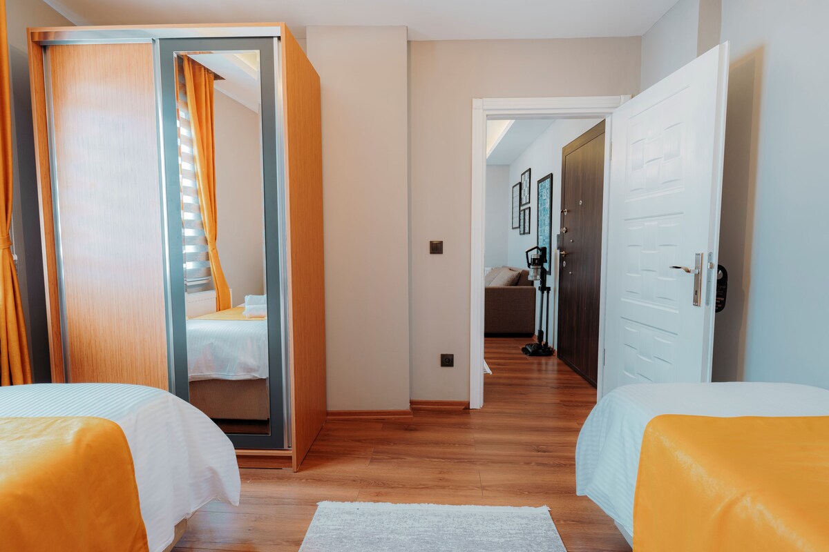 Habitació d'hotel amb dos llits, un sòl de fusta, una catifa blanca i un passadís que condueix a un bany.