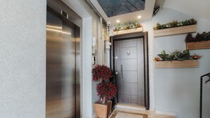 A modern entryway with a dark wooden door, a small wooden side table with a potted plant, and a ceiling with a skylight. - Umut Apartments (Trabzon)