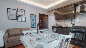 A modern kitchen with a black stove, white cabinets, and a dining area set with white tableware and chairs. - Umut Apartments (Trabzon)