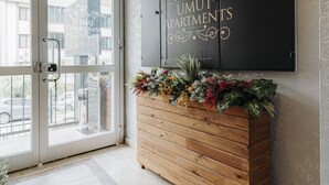 A reception area with a wooden bench, a black sign with gold lettering, and a view through glass doors. - Umut Apartments (Trabzon)