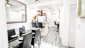 Una cocina moderna con gabinetes blancos, una zona de comedor con mesa y sillas, y un ventilador de techo.