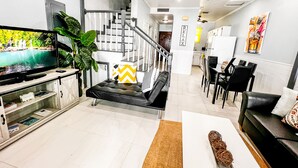 Una sala de estar moderna con televisor de pantalla plana, una escalera, una zona de comedor y una cocina.