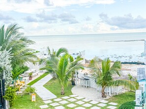 A beachfront property with a paved walkway, palm trees, and a view of the sea.