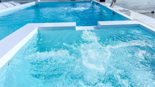 Una piscina con agua cristalina, rodeada de una terraza blanca y palmeras, con vistas al océano.
