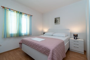 Une chambre à coucher comprenant un lit, des tables de chevet, une commode, une fenêtre avec des rideaux et un tableau accroché au mur.