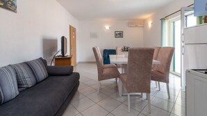 A modern living room with a grey sofa, a dining area with a white table and chairs, and a kitchen area with a fridge. - IGNACIJA 1 - Apartment 3+1 people, sea view terrace (Okrug Gornji)