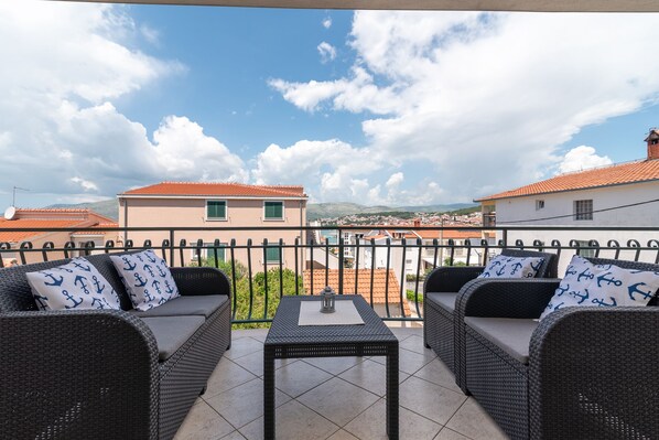 A balcony with wicker furniture and a table, overlooking a town with red-roofed buildings and a clear sky. - IGNACIJA 1 - Apartment 3+1 people, sea view terrace (Okrug Gornji)