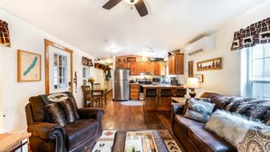 A spacious living room with leather sofas, a coffee table, and a dining area with a kitchen in the background.