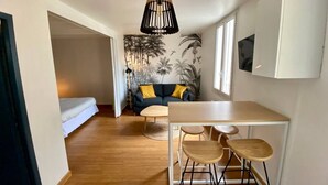 A compact living space with a sofa, a dining table with chairs, a hanging light fixture, and a wall with a tropical mural. - Magnificent T3 apartment in the heart of Bordeaux (Bordeaux)