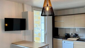 A compact kitchen with a dining area, a built-in dishwasher, and a flat-screen TV mounted on the wall.