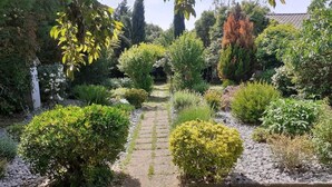 A garden with a stone pathway, various shrubs, and trees. - Charming gîte in a green setting with swimming pool South Ardèche (Berrias-et-Casteljau)