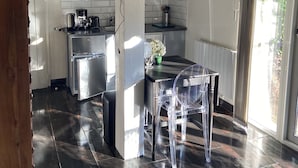 A modern kitchen with a flat-screen TV, stainless steel appliances, and a dining area with clear chairs. - Charming gîte in a green setting with swimming pool South Ardèche (Berrias-et-Casteljau)
