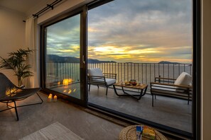 Un balcon offrant une vue sur la mer et les montagnes au coucher du soleil.