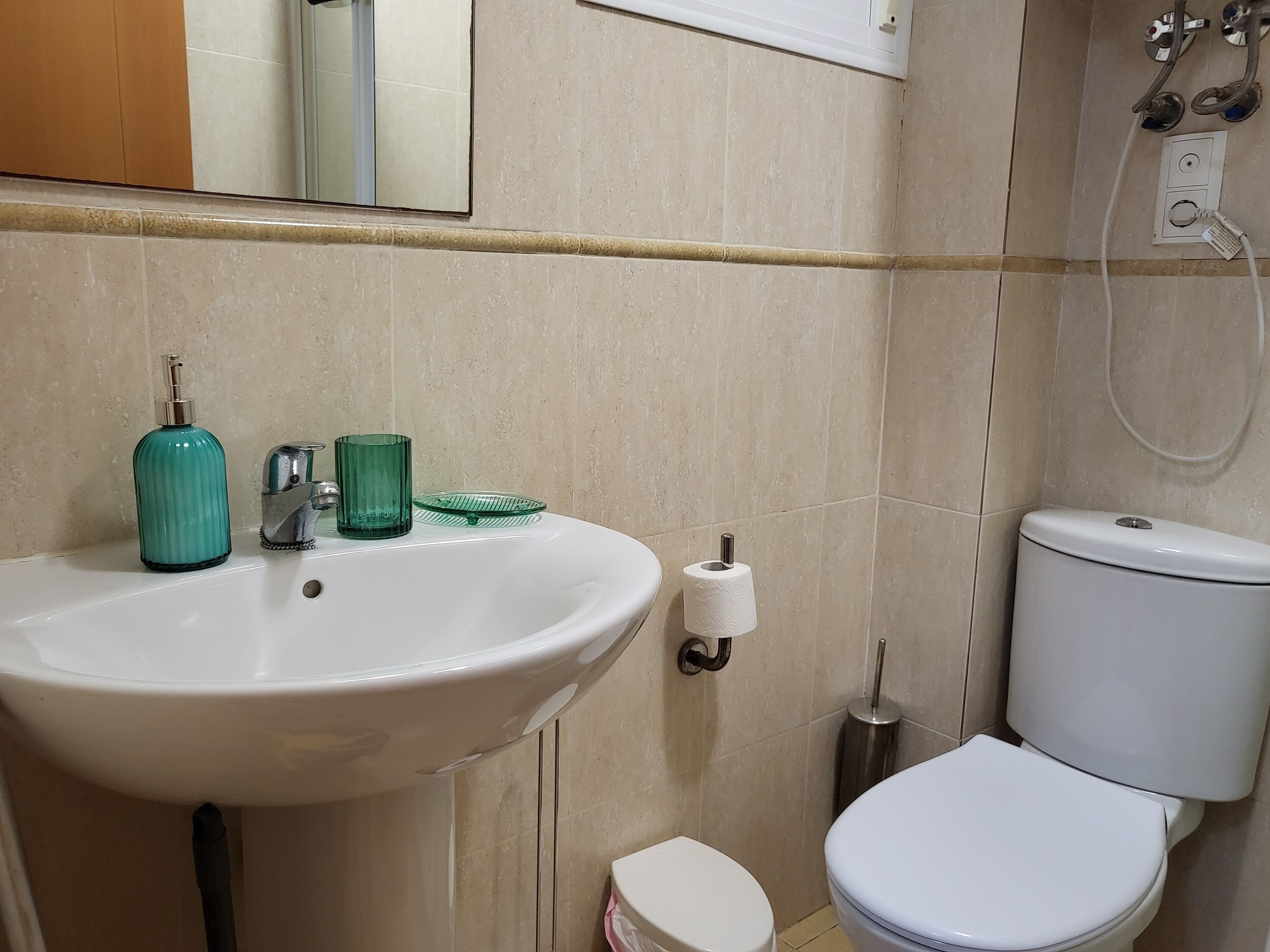 Une salle de bain avec un lavabo blanc, un distributeur de savon vert et des toilettes.