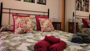 Ein Hotelzimmer mit einem Bett, das mit tropisch gestalteter Bettwäsche, einem Metall-Kopfschild und floralen Kissen ausgestattet ist.